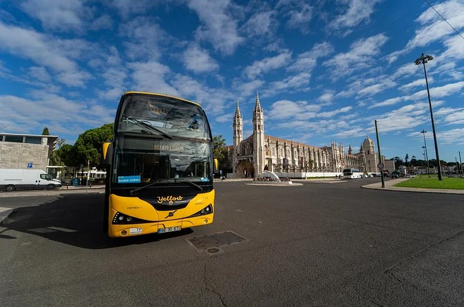 A yellow double-decker sightseeing bus parked by the Jerónimos Monastery